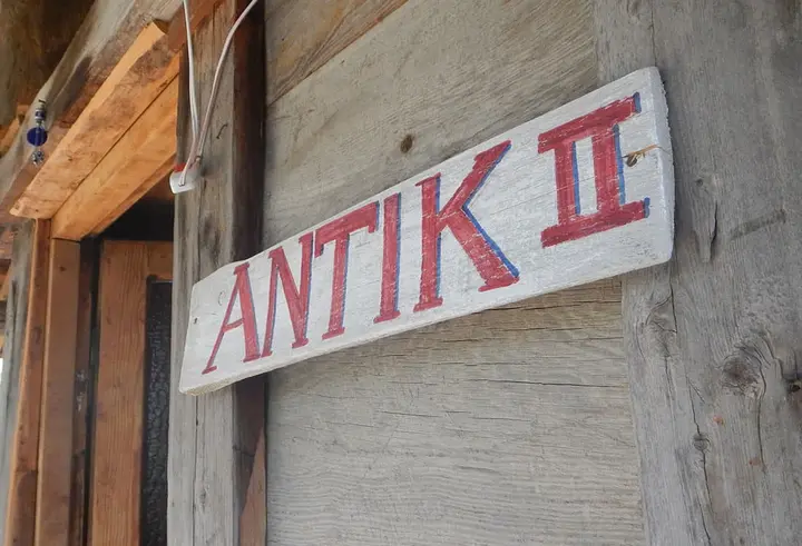 Yıpranmış ahşap duvarda elle boyanmış Antik II tabelası