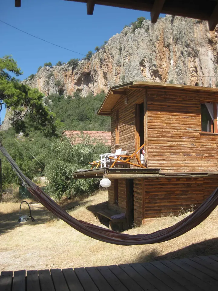Terasta gerilmiş hamak, arkada bungalov ve kayalık