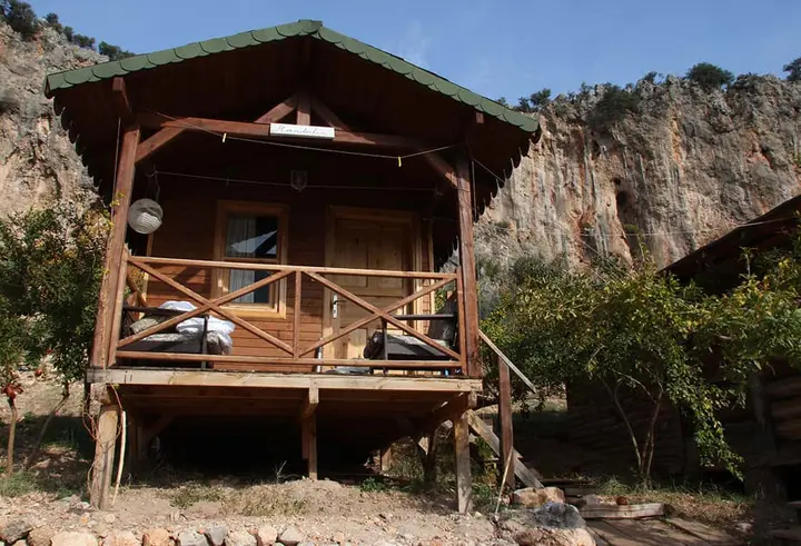 Kazıklar üzerinde korkuluklu Mandalin bungalovu, arkada kayalık