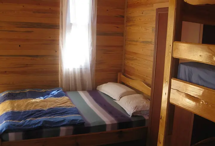 Doppelbett mit gestreifter Decke am Fenster im Bungalow Nar