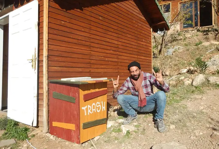 Man making a rock gesture beside a painted wooden trash bin